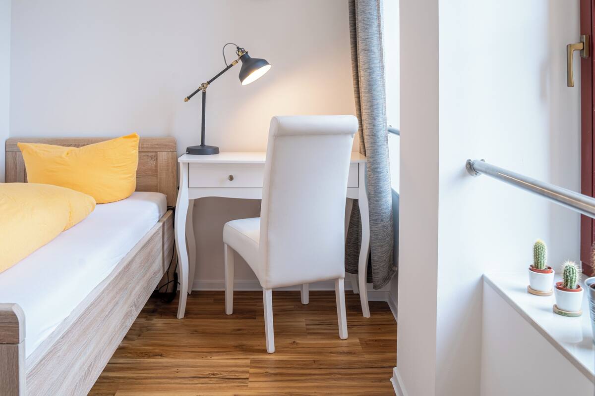 A bedroom with a bed, a desk, a chair, a lamp, and a window with curtains.