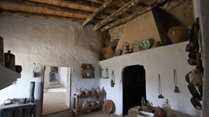 Una cocina rústica con estufa de madera, repisas llenas de cerámica y una chimenea.