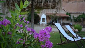 Un patio con dos sillones de descanso, una estructura cubierta de paja y un edificio con techo de tejas al fondo.