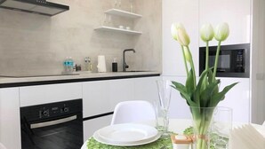 A modern kitchen with white cabinets, a black oven, and a dining area with a white table set for two. - PaulMarie Apartments in Bobruisk (Bobruysk)