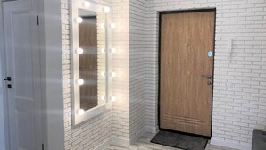 A hallway with a white brick wall, a wooden door, and a mirror with lights. - PaulMarie Apartments in Bobruisk (Bobruysk)