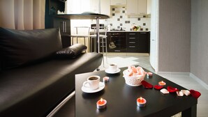 A modern living room with a black leather sofa, a coffee table with a cake and candles, and a view of a kitchen in the background. - PaulMarie Apartments in Bobruisk (Bobruysk)