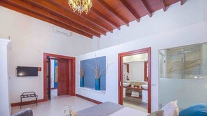 A bedroom with a bed, a TV, a window with decorative vases, and a bathroom visible through an open door. - Delmás Hotel Emblemático (Haria)