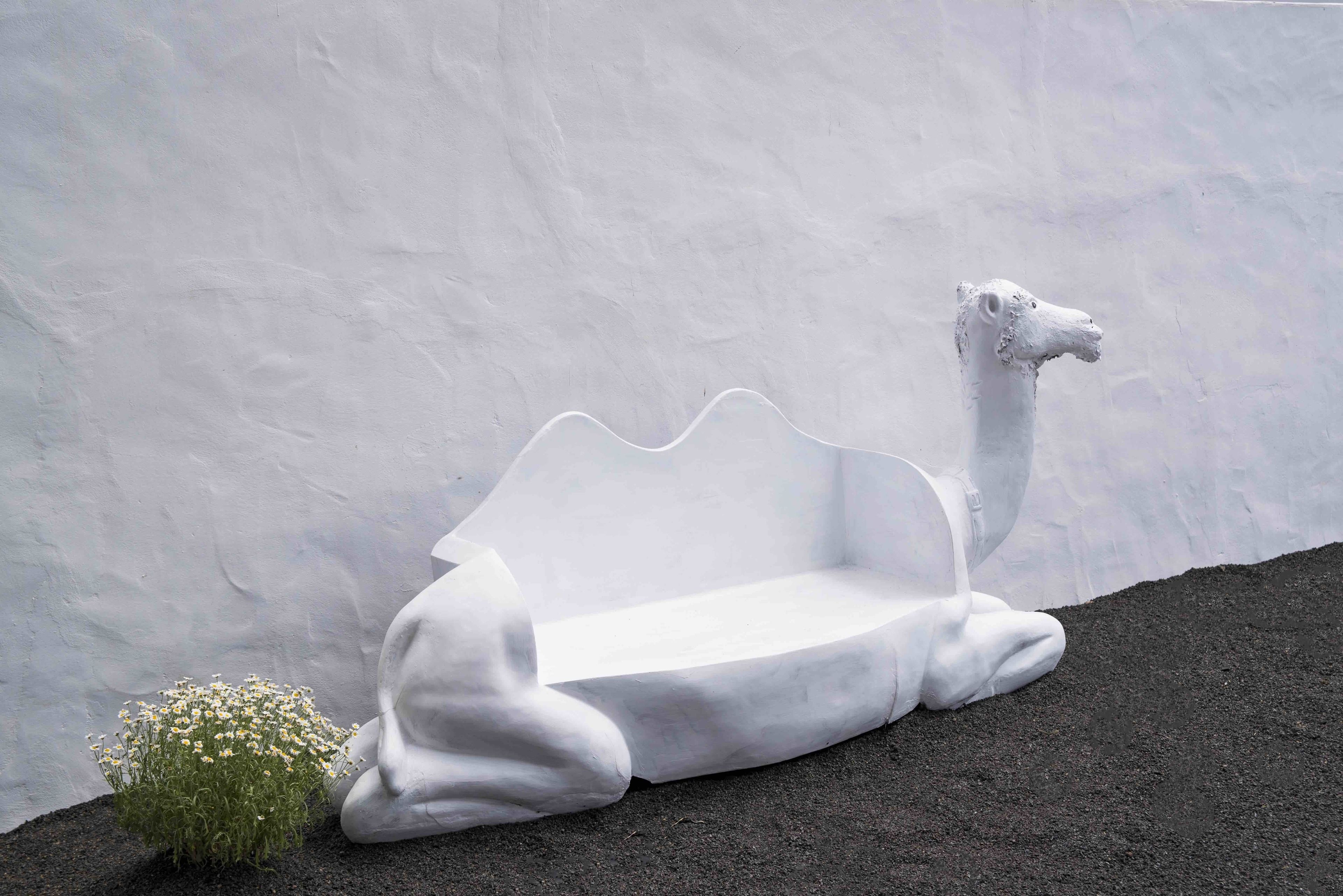 A white, sculptural bench against a textured wall.