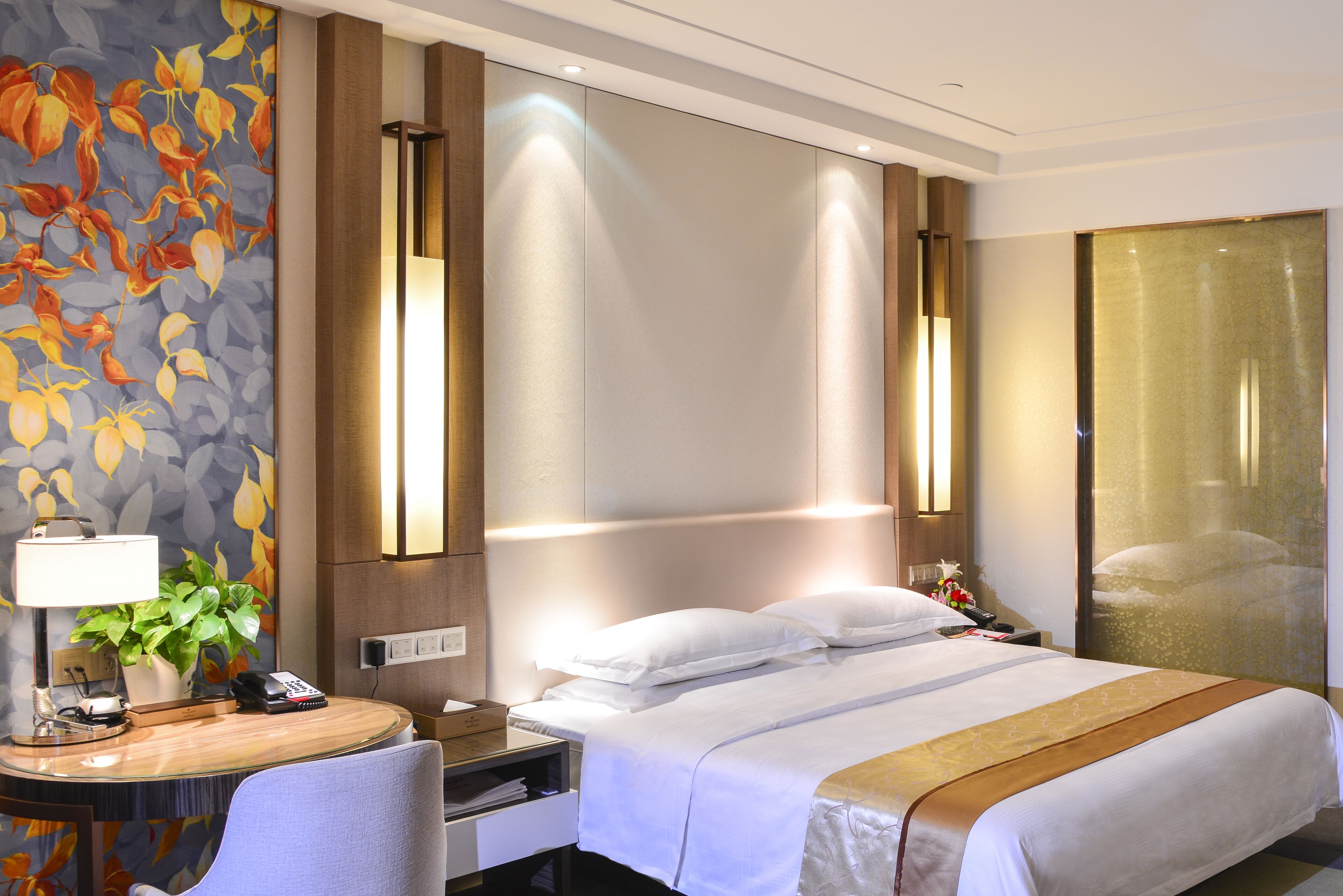 A hotel room with a bed, bedside table, lamp, and a floral wall mural.