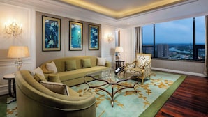 A spacious living room with a green sofa, a glass coffee table, and a decorative chair. There are three framed artworks on the wall and a chandelier.