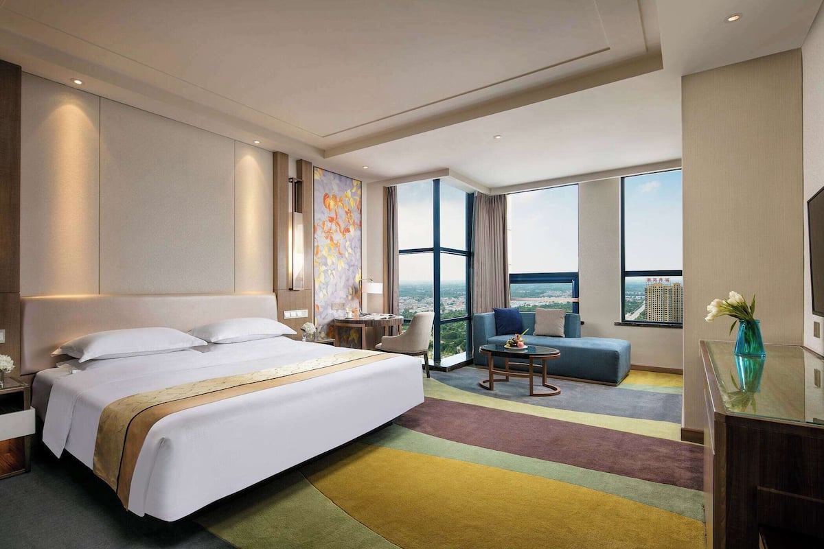 Una habitación de hotel moderna con una cama grande, un sofá, una mesita y vistas a la ciudad.