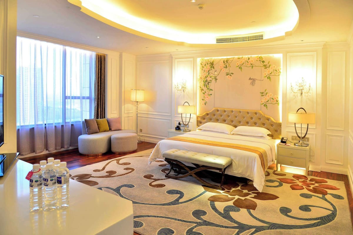 Habitación de hotel con una cama grande, un sofá, un banco y un escritorio con botellas de agua.