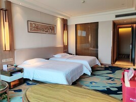 Habitación de hotel con dos camas, una mesita de noche, una lámpara, una obra de arte en la pared y una puerta que da a otra habitación.