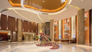 A spacious lobby with a modern design, featuring a reception desk, seating area, and a decorative floral arrangement on the floor.