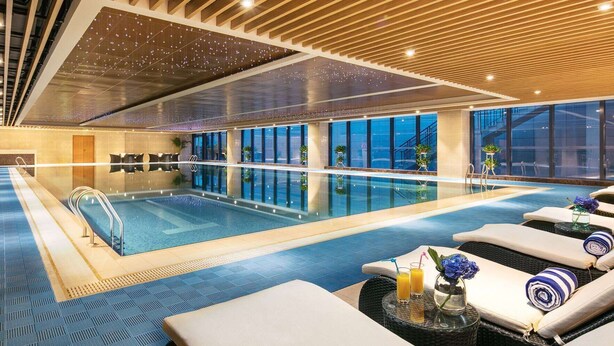 An indoor swimming pool with lounge chairs and a glass wall.