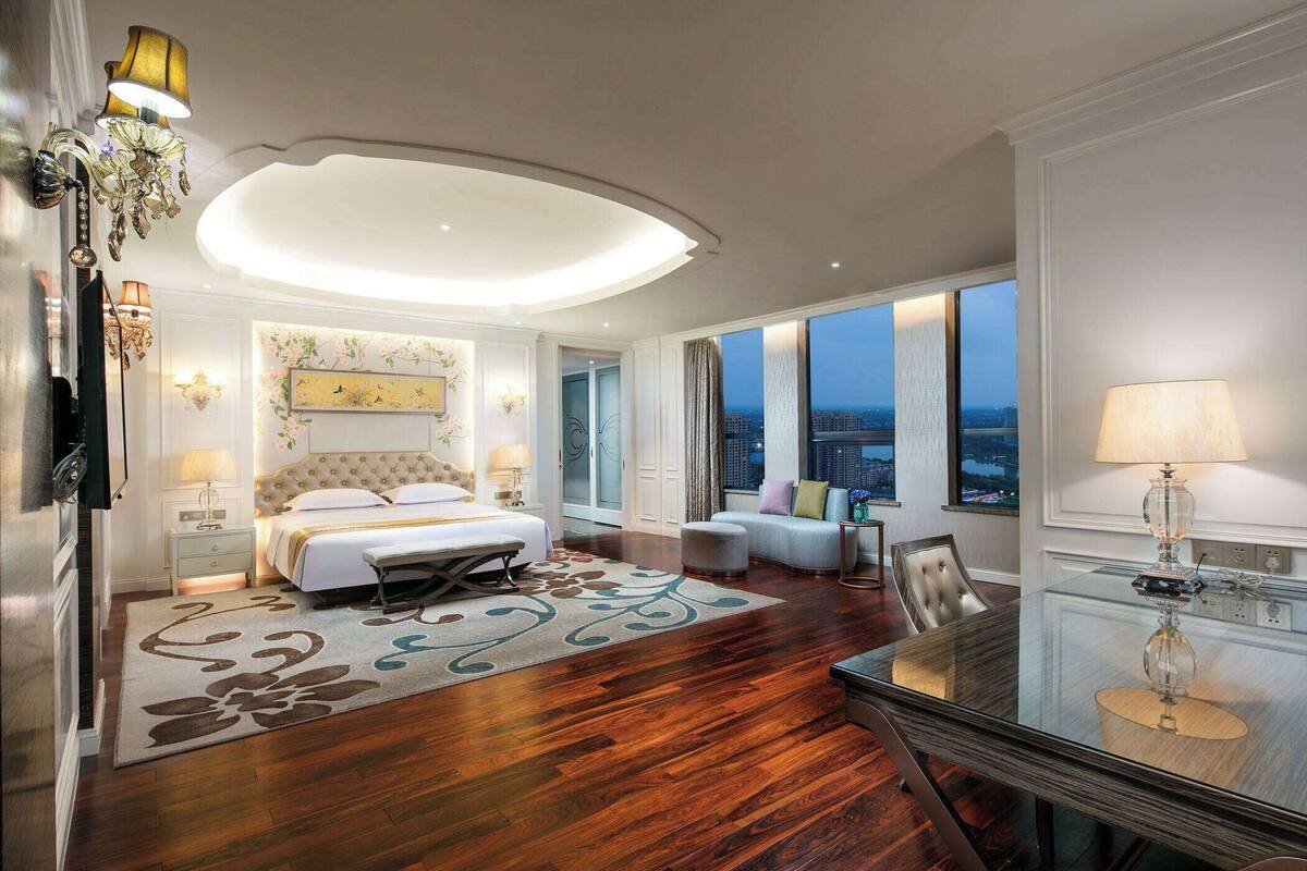 Un dormitorio amplio con una cama grande, una mesa de comedor de vidrio y vistas a la ciudad.