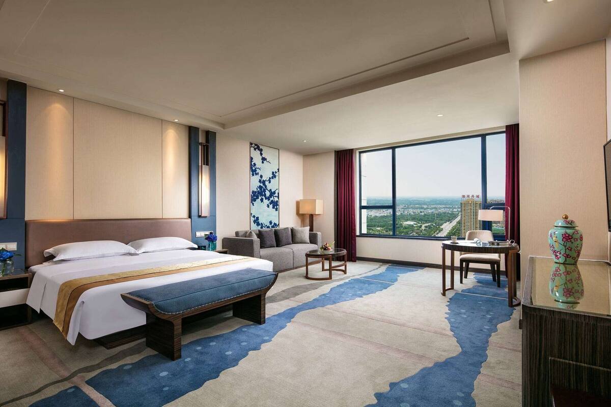 Habitación de hotel con una cama grande, un sofá, una mesita y vistas a la ciudad.