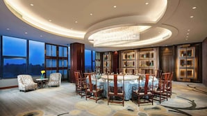 A spacious dining area with a round table and chairs, large windows with a view, and a chandelier.