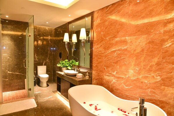A modern bathroom with a freestanding bathtub, a glass shower enclosure, a marble-tiled wall, and a large mirror. - Ramada Heze (Heze)