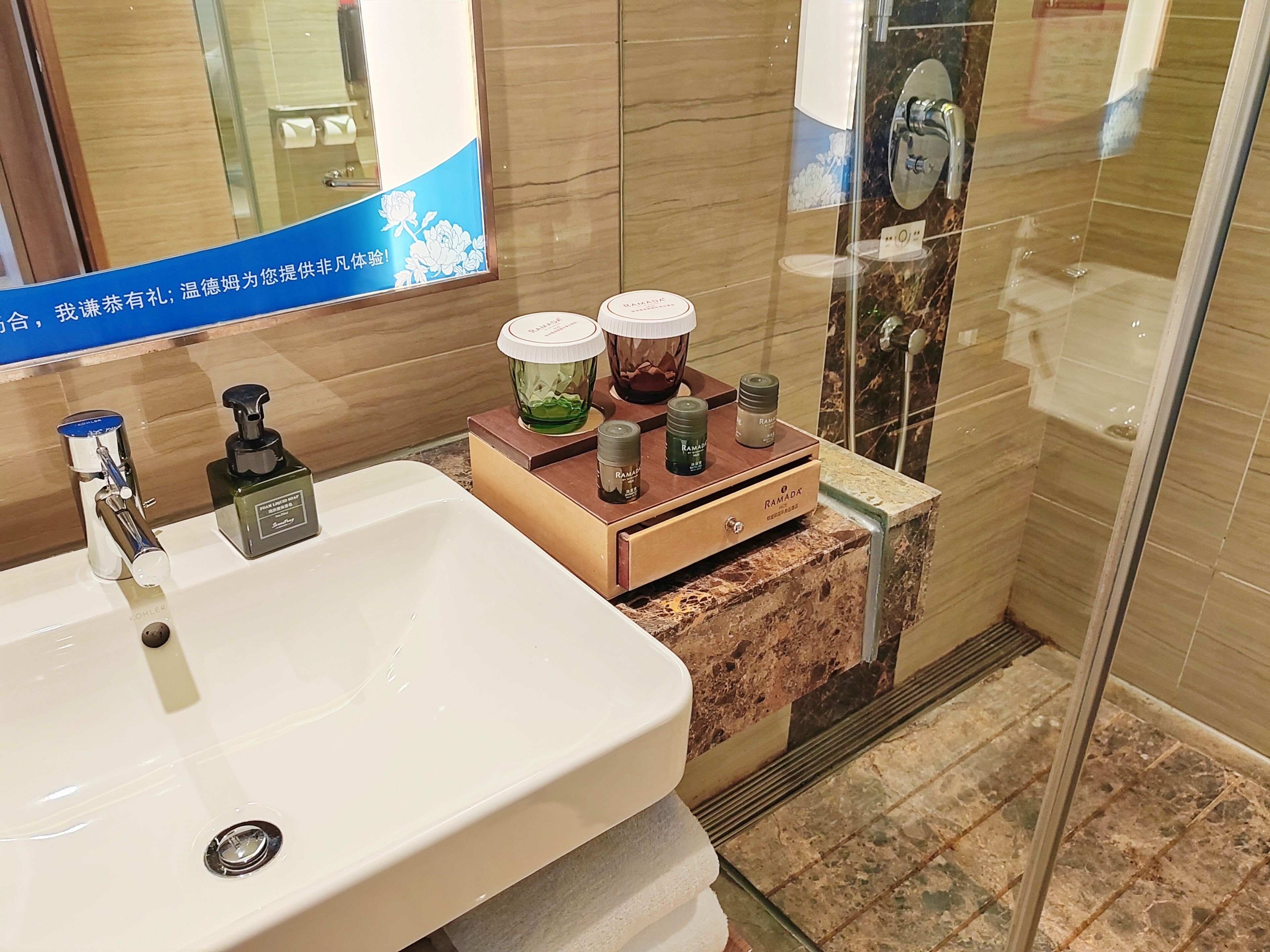 A bathroom with a white sink, a mirror, and a glass shower enclosure. There are toiletries on a wooden tray.