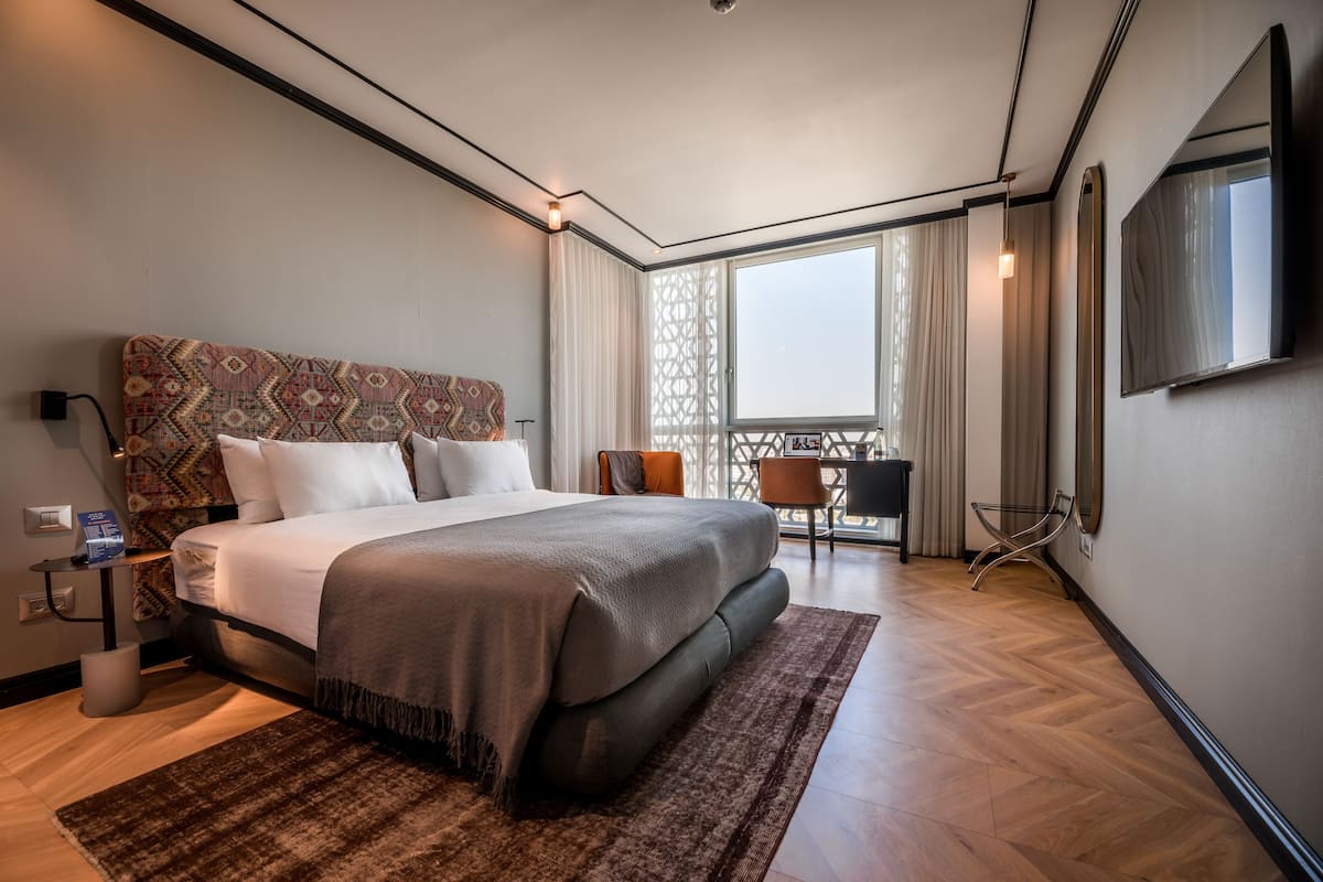 A modern hotel room with a large bed, a desk, and a balcony with curtains.