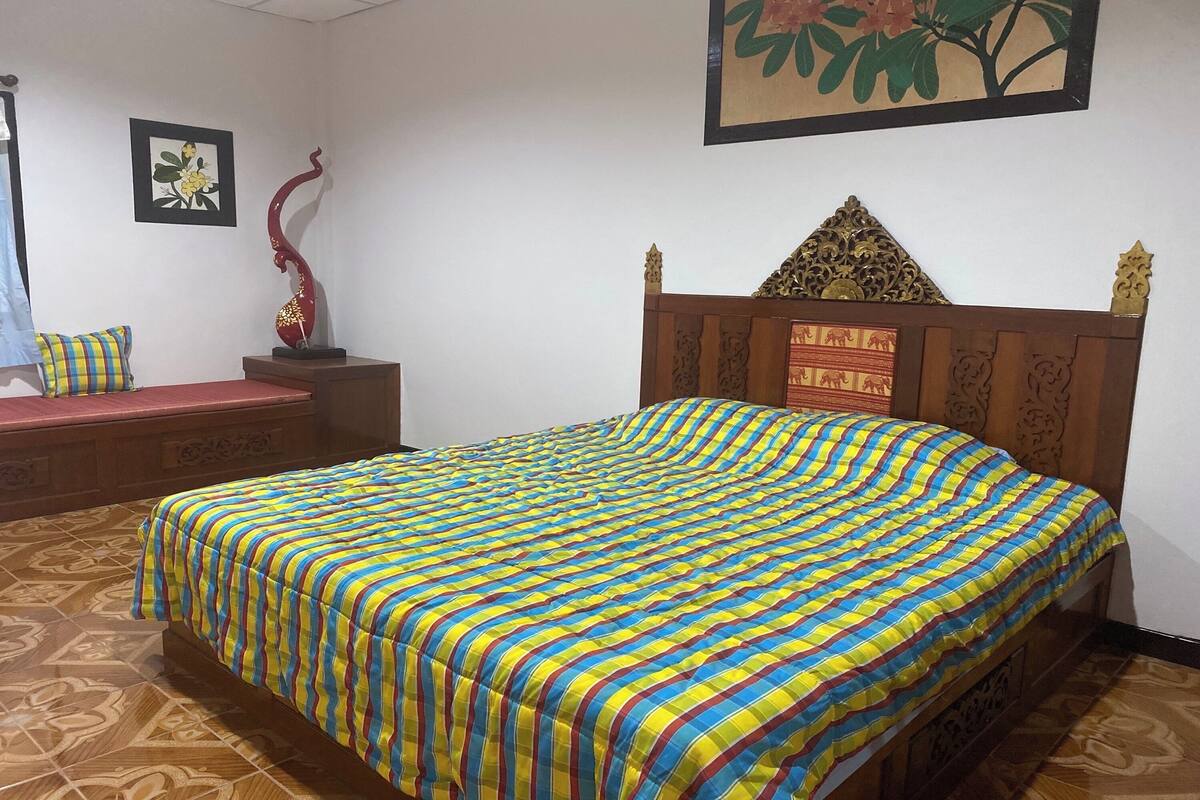A room with a bed, a wooden headboard, a bench, and a decorative sculpture.