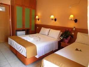A hotel room with two beds, a wooden wardrobe, a small desk, and a nightstand with a lamp.