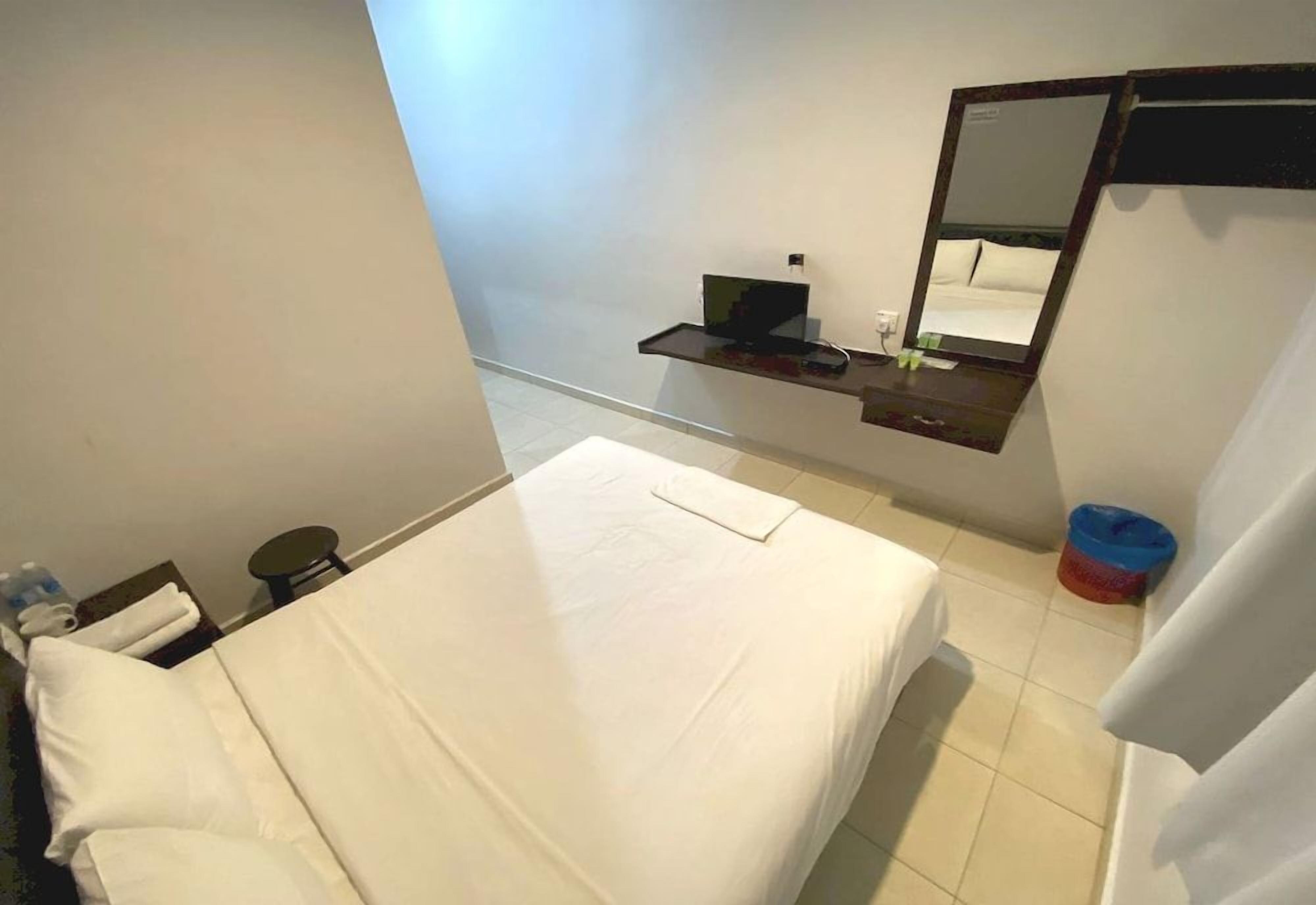 A hotel room with a bed, a bedside table, a mirror, and a small shelf.