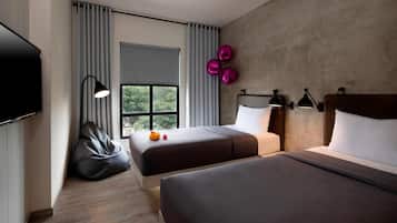 A modern hotel room with two beds, a large window with curtains, a flat-screen TV, and a bean bag chair.