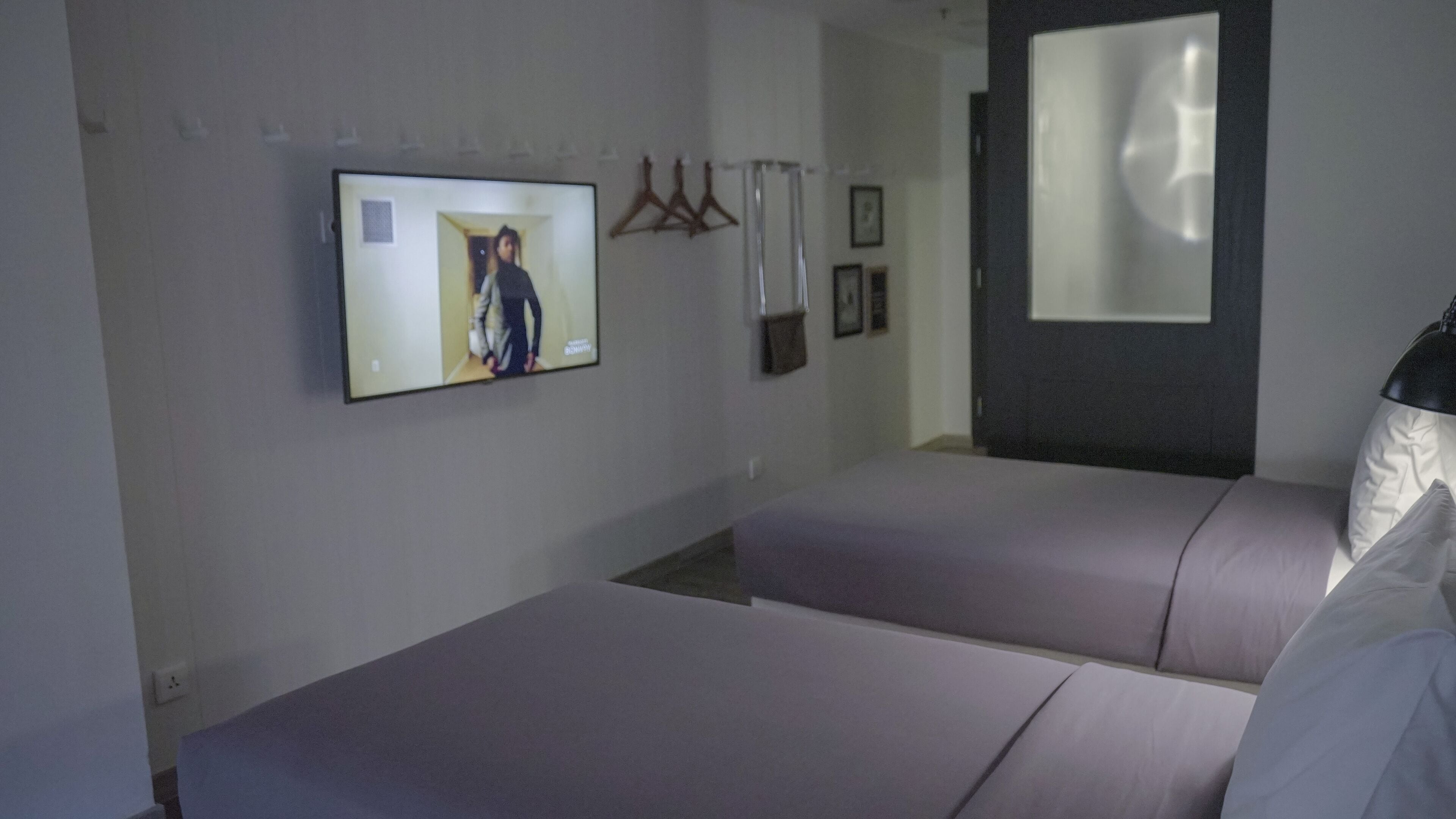 Une chambre d’hôtel avec deux lits, un téléviseur fixé au mur, un porte-manteau et un miroir.