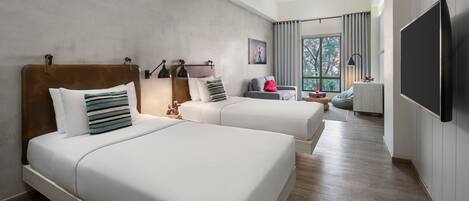 A hotel room with two beds, a TV, a desk, and a view of the outdoors.