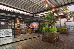 Un bar situé sur le toit, doté d’une terrasse en bois, de tabourets de bar et d’un panneau lumineux au néon.