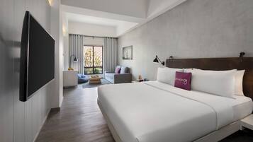 A modern hotel room with a large bed, a flat-screen TV, a sofa, and a dining area.