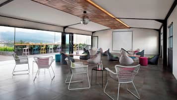 A spacious indoor area with a high ceiling, large windows offering a view of the outdoors, and a mix of seating arrangements including chairs and bean bags.