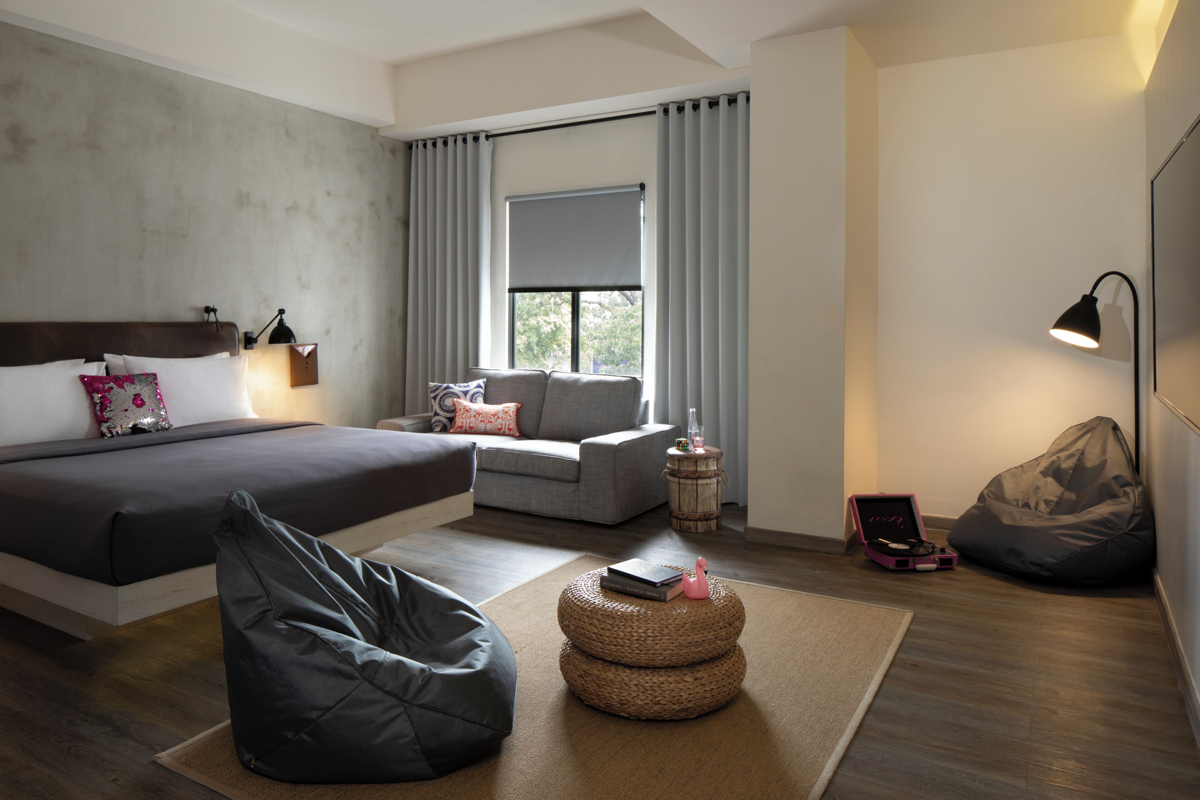 Une chambre moderne avec un lit, un canapé, un fauteuil poire, une petite table ronde et un pouf.