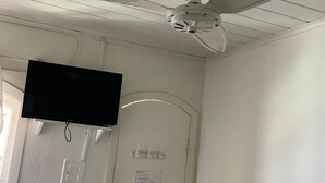 A room with a ceiling fan, a mounted television, a door with a sign, and a light switch.