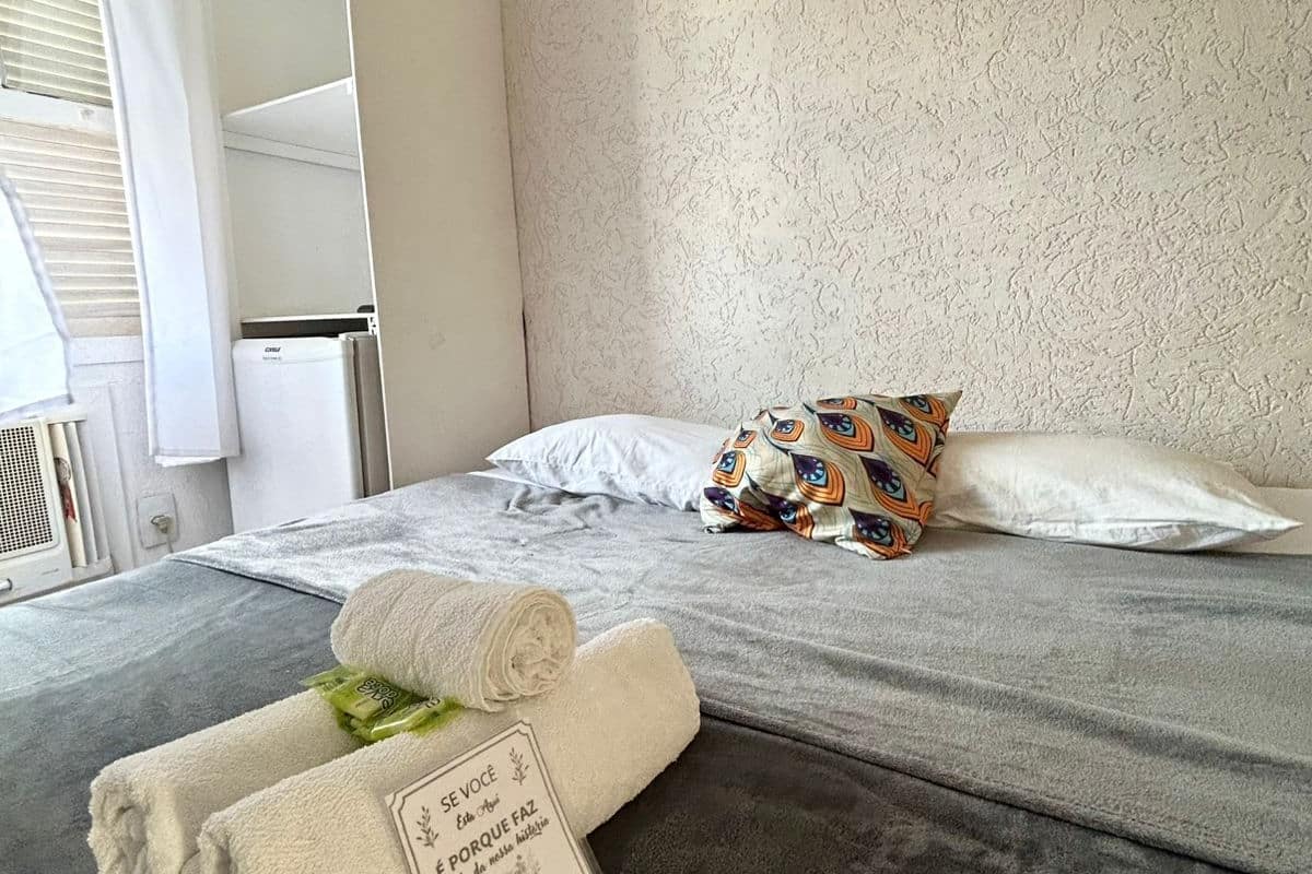 A hotel room with a bed, pillows, a towel, and a sign.