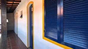 A corridor with a tiled floor, a wooden ceiling, and a blue shuttered window. - Pousada Aldeia Buzios (Búzios)