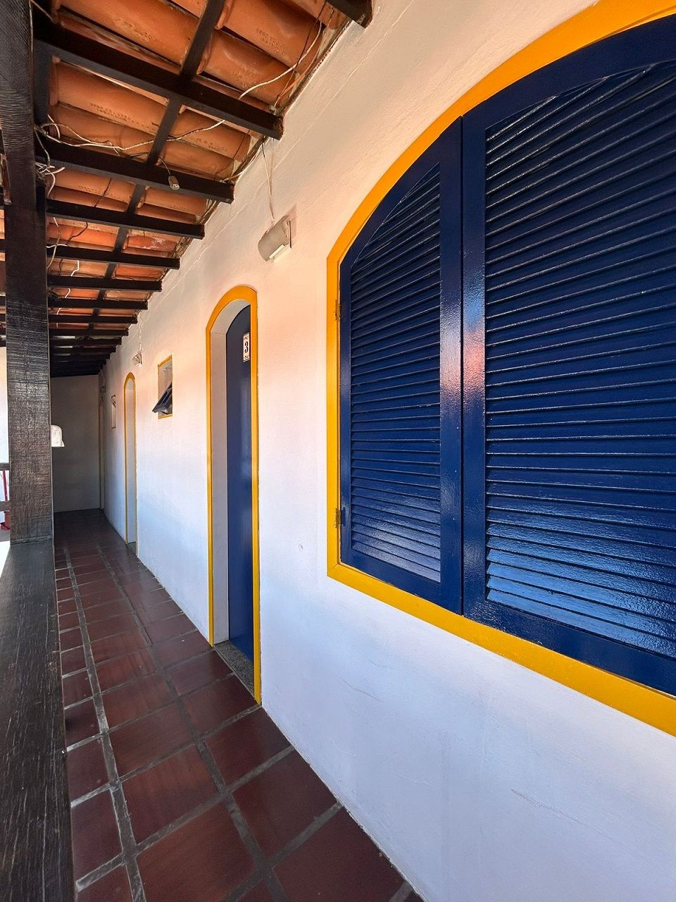 A corridor with a tiled floor, a wooden ceiling, and a blue shuttered window.