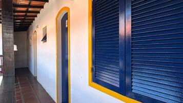A corridor with a tiled floor, a wooden ceiling, and a blue shuttered window.