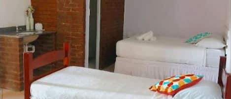 A single bed with a colorful pillow, a wooden headboard, and a ceiling fan in a room with a brick wall and a white door.