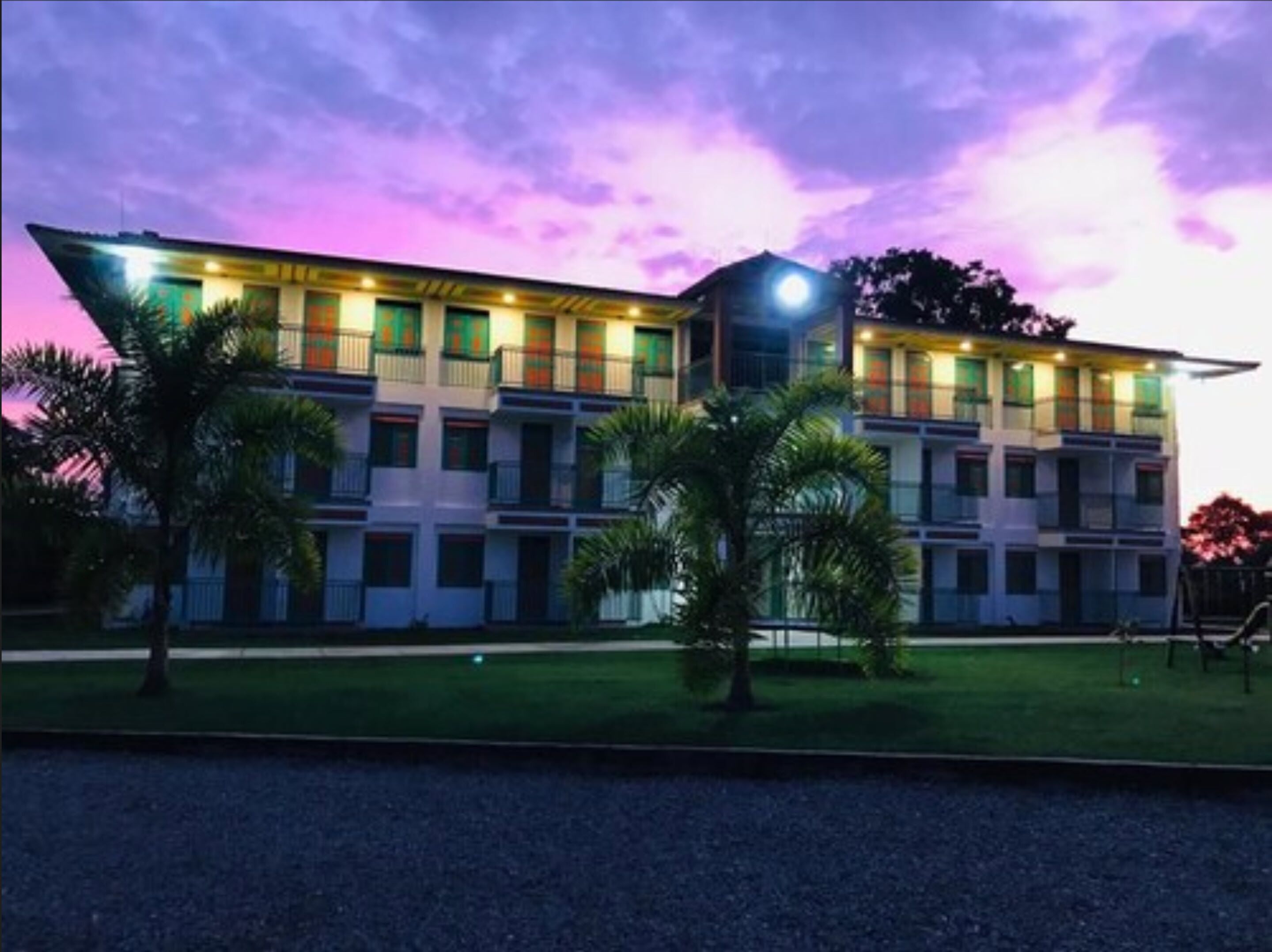 A modern hotel with a flat roof, multiple balconies, and a well-maintained lawn.