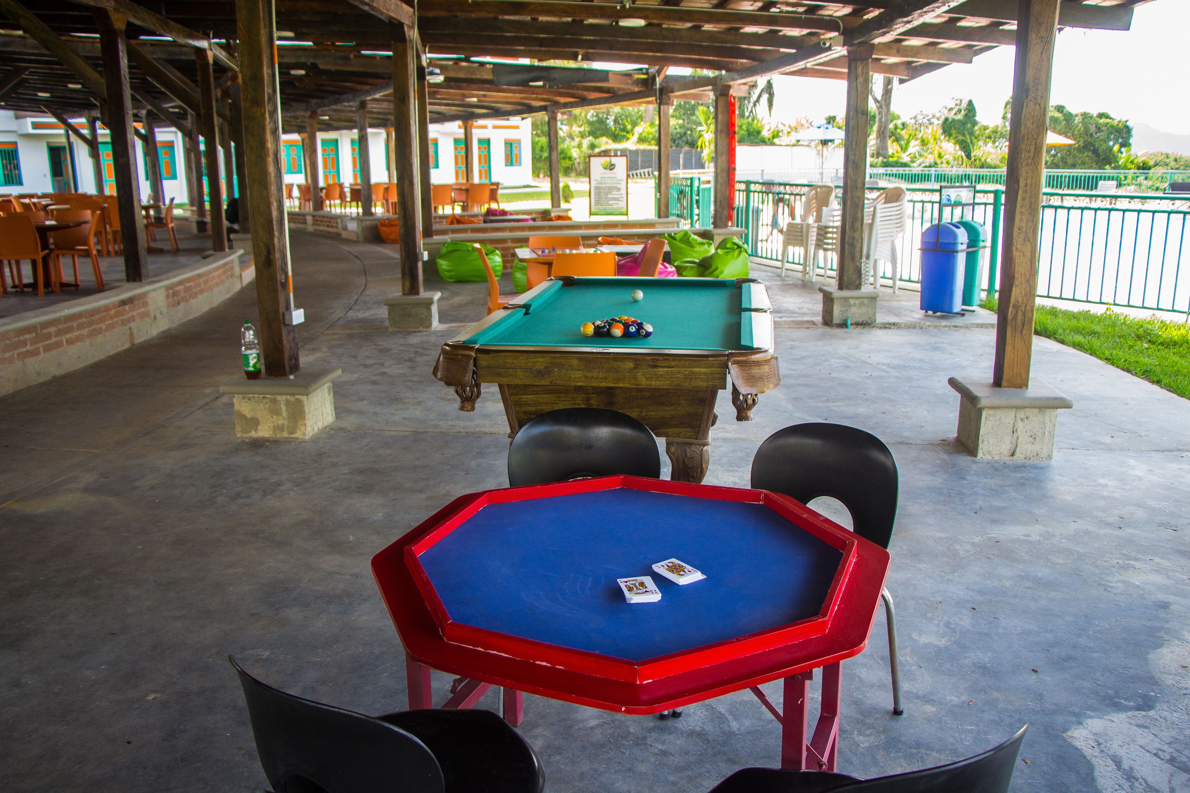 An outdoor pool table area with a red table and chairs, surrounded by a covered seating area with orange chairs.