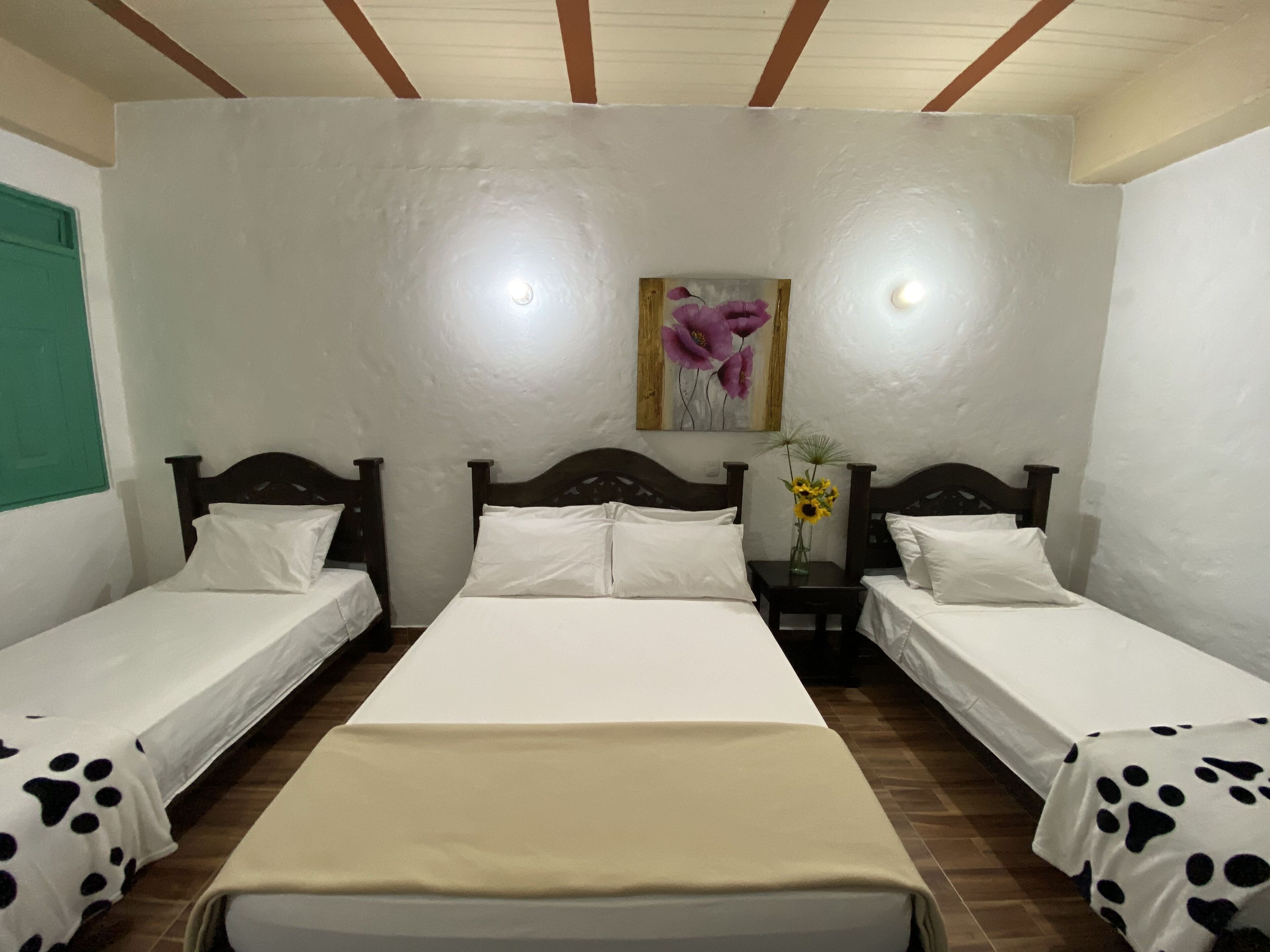 A room with two single beds, a wooden headboard, a nightstand with a vase of sunflowers, and a painting on the wall.
