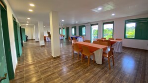 Un espacio interior amplio con varias mesas y sillas, un cuadro en la pared y ventanas grandes con vistas a zonas verdes.