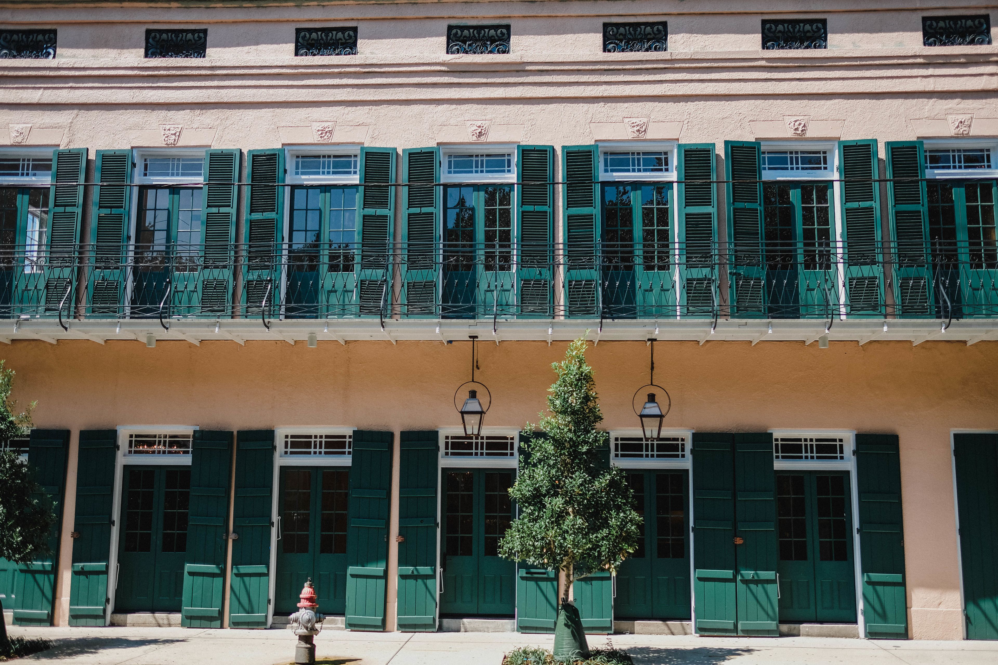 A building with multiple green shutters and windows, a fire hydrant, and a tree in front.
