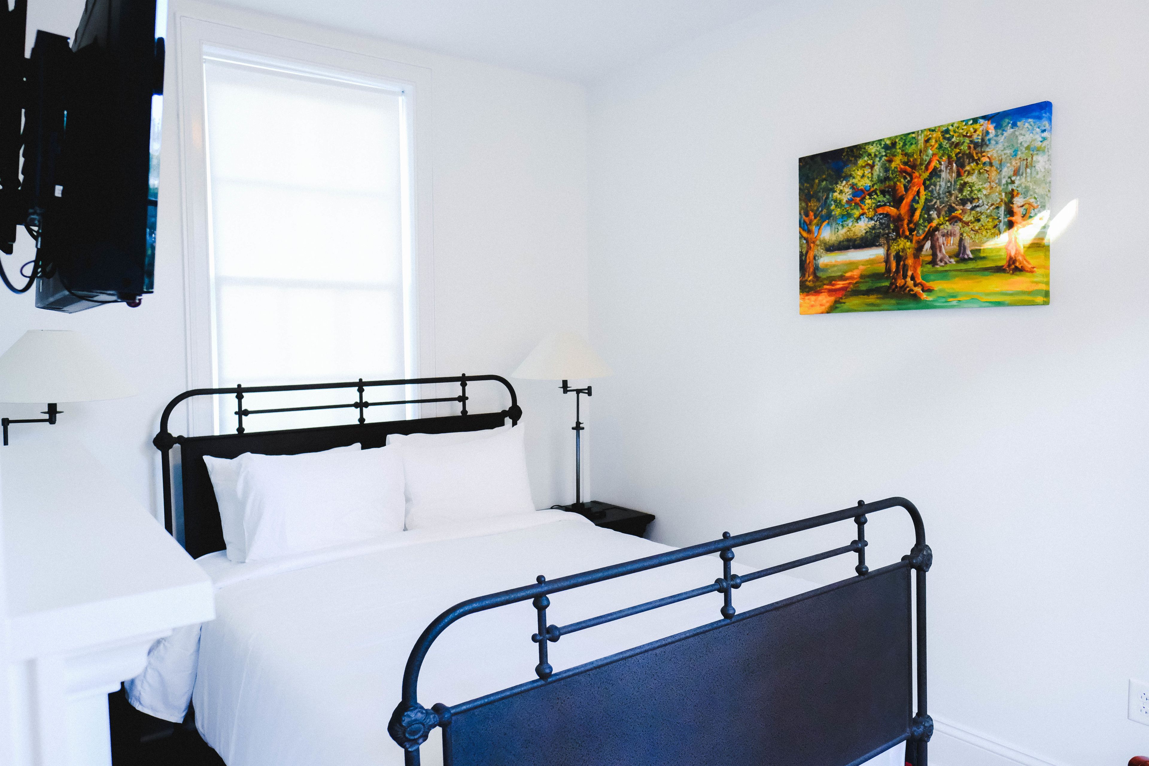 A bedroom with a single bed, a nightstand, a lamp, and a painting on the wall.