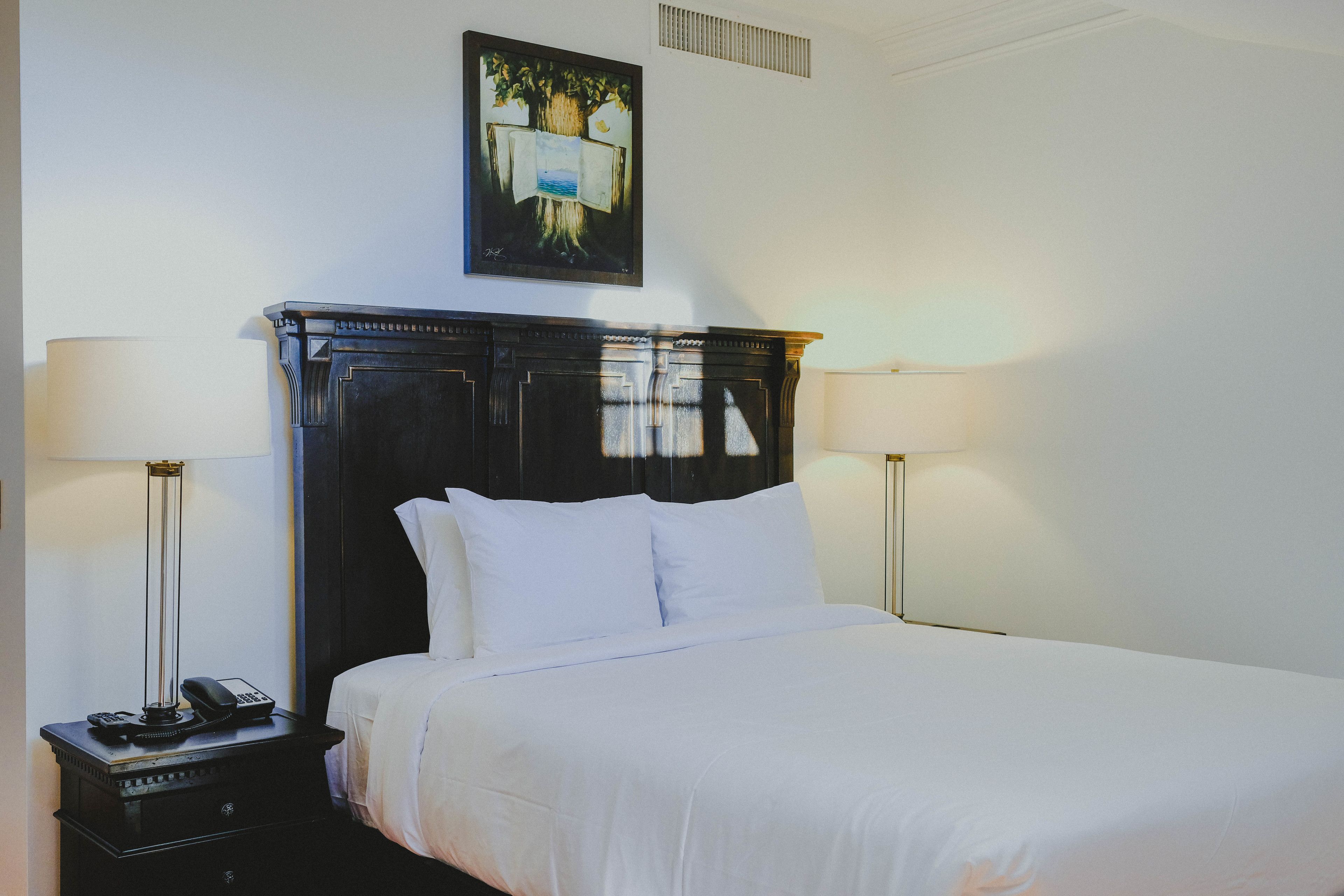 A neatly made bed with white linens, a dark wooden headboard, and two bedside lamps.