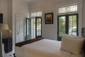 Une chambre à coucher comprenant un lit, une table de chevet, une lampe et deux portes donnant sur un balcon.