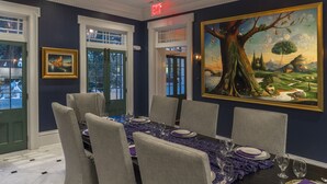 Uma sala de jantar com uma mesa grande posta para seis pessoas, obras de arte emolduradas na parede e um lustre.