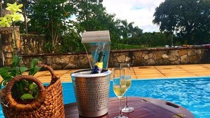 Escena junto a la piscina con un dispensador de bebidas, una cesta tejida y dos vasos de una bebida amarilla.
