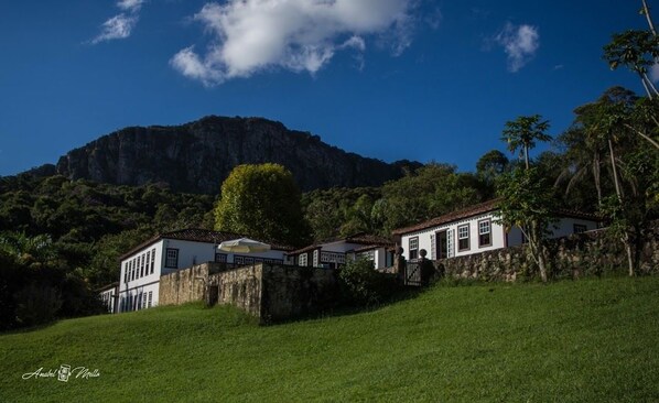 A white building with a red roof, surrounded by lush greenery and a stone wall.