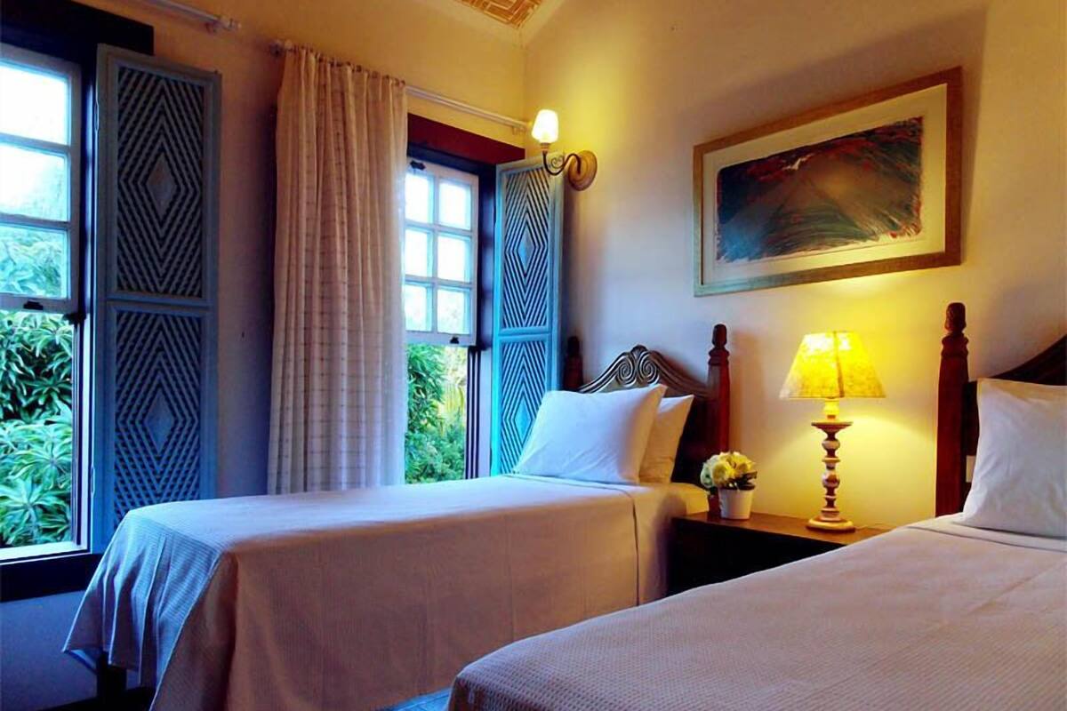Une chambre d’hôtel avec deux lits, un tableau au mur, une fenêtre avec des rideaux et une table de chevet avec une lampe.