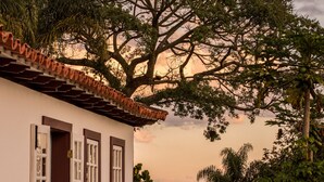 Un edificio blanco con puerta y ventanas rojas, rodeado por un camino de piedra y un muro de piedra.